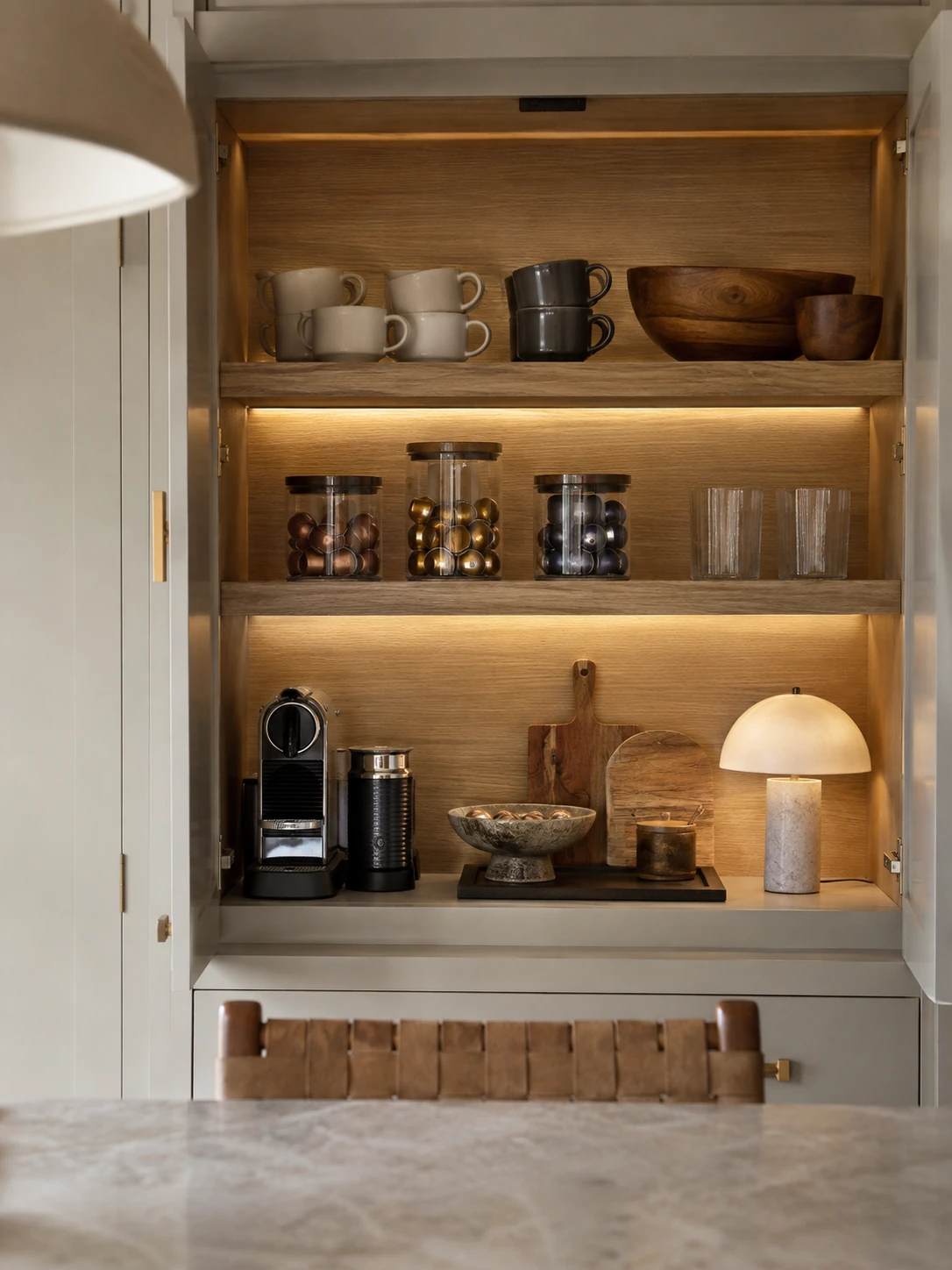 Built-in cabinet coffee station with warm wood shelving, stacked mugs and coffee machine