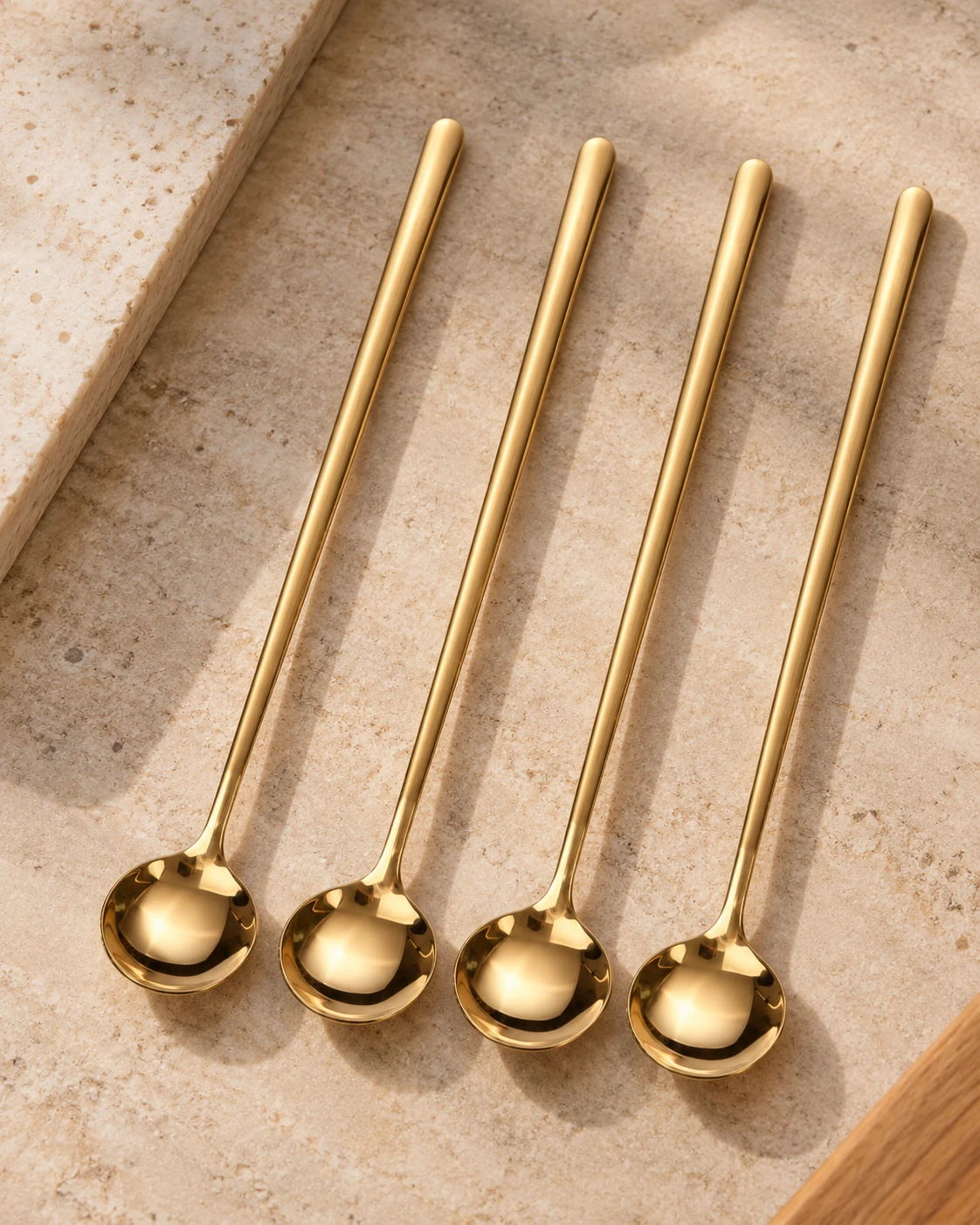 Set of four long-handle gold coffee spoons arranged on a warm neutral stone surface